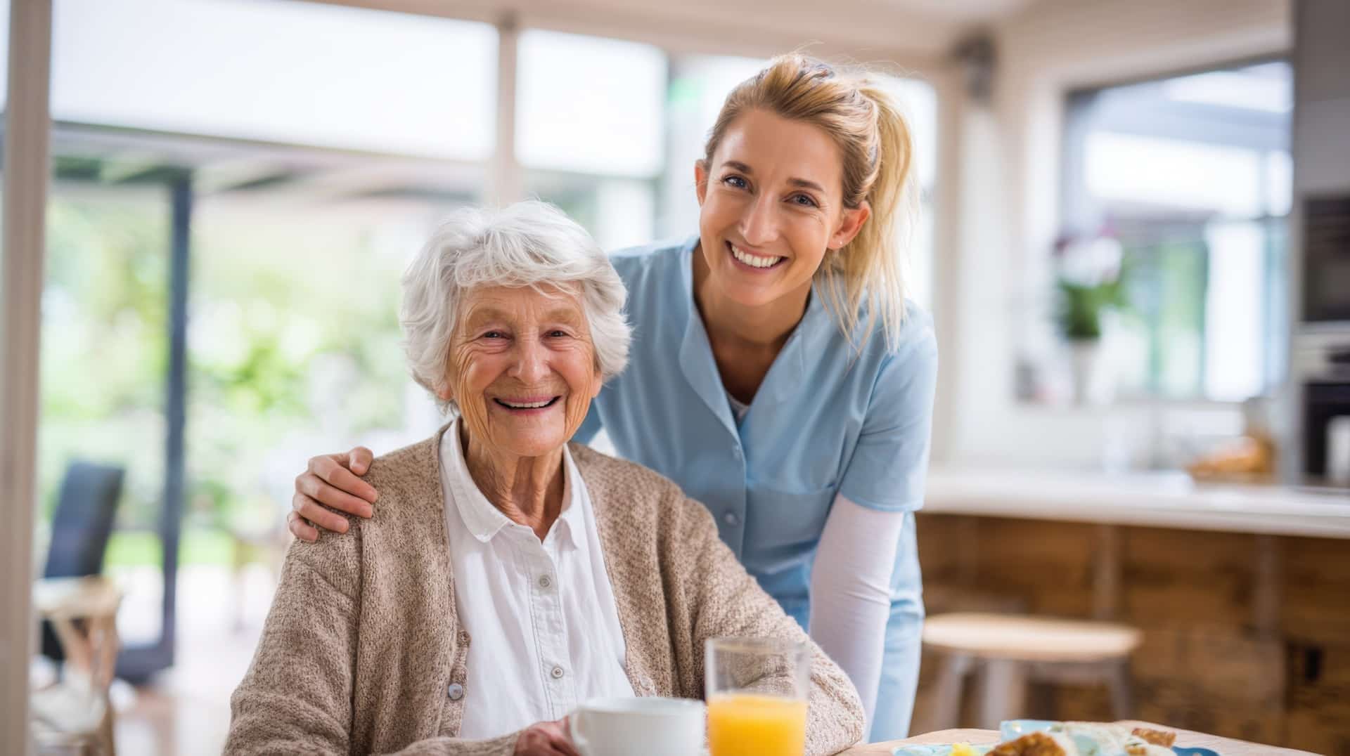 Pflegekraft frühstückt mit lächelnder Seniorin am Tisch | Pflegehelfer Frankfurt